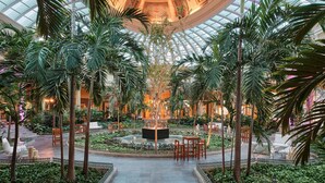 A spacious atrium with a high glass ceiling, surrounded by lush greenery and palm trees. - JOIA Paraíso by Iberostar - Adults Only - All Inclusive (Playa del Carmen)
