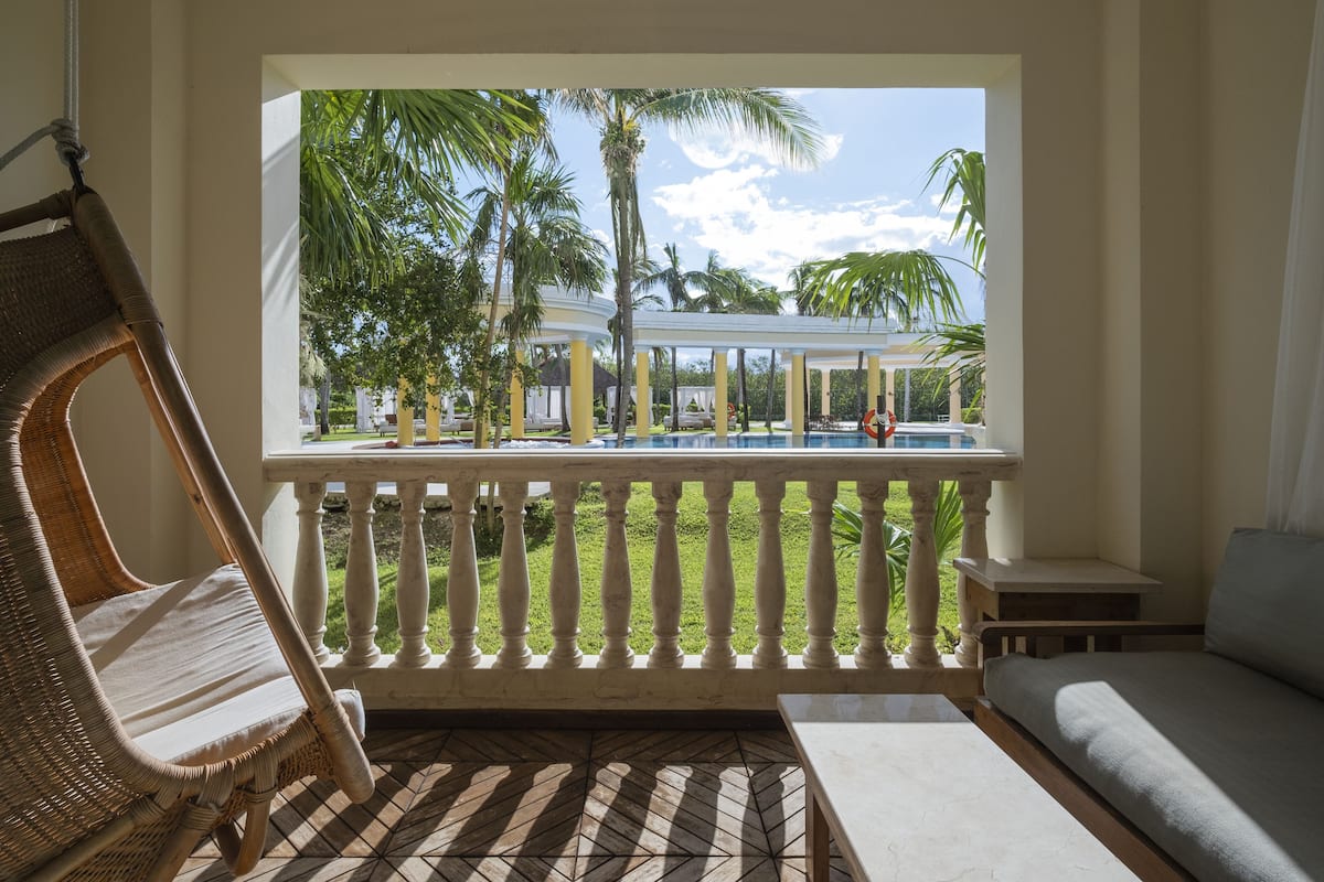 A balcony with a wicker chair, a sofa, and a view of a pool and palm trees.