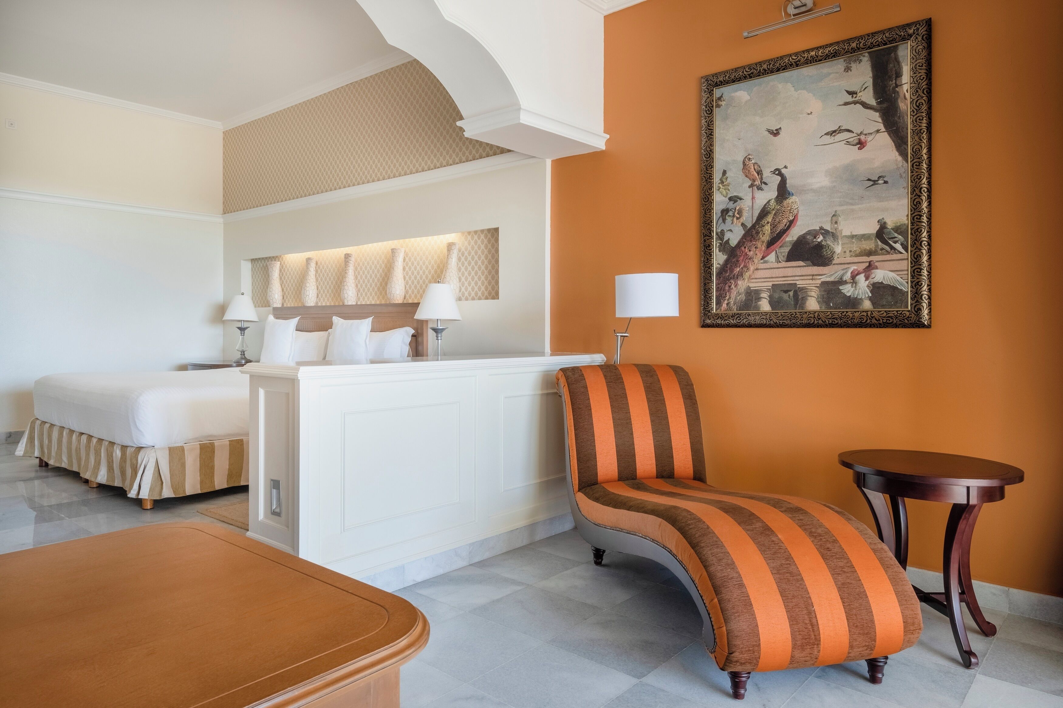 A hotel room with a bed, a sofa, a small table, and a painting on the wall.