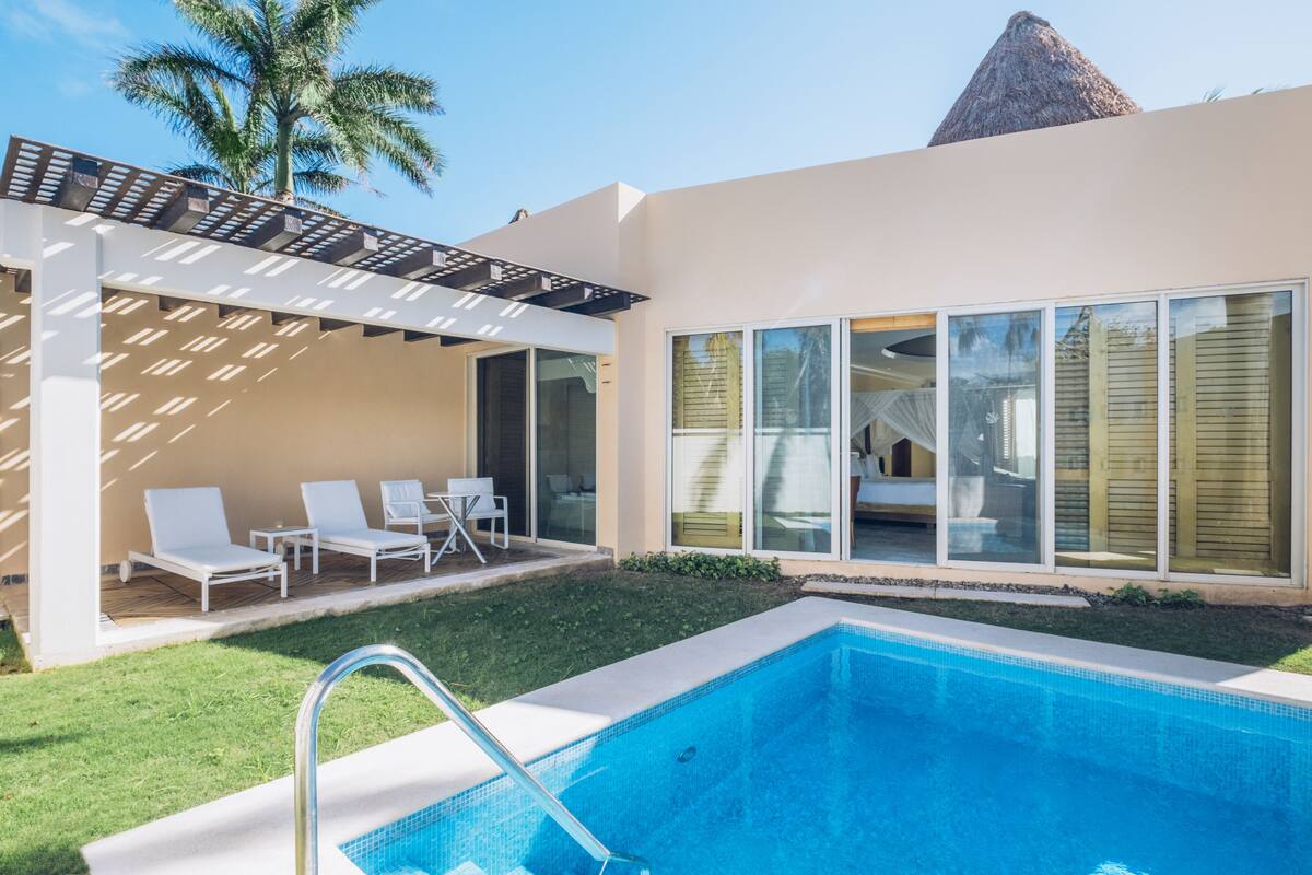 A modern poolside area with a clear blue pool, white lounge chairs, and a pergola.
