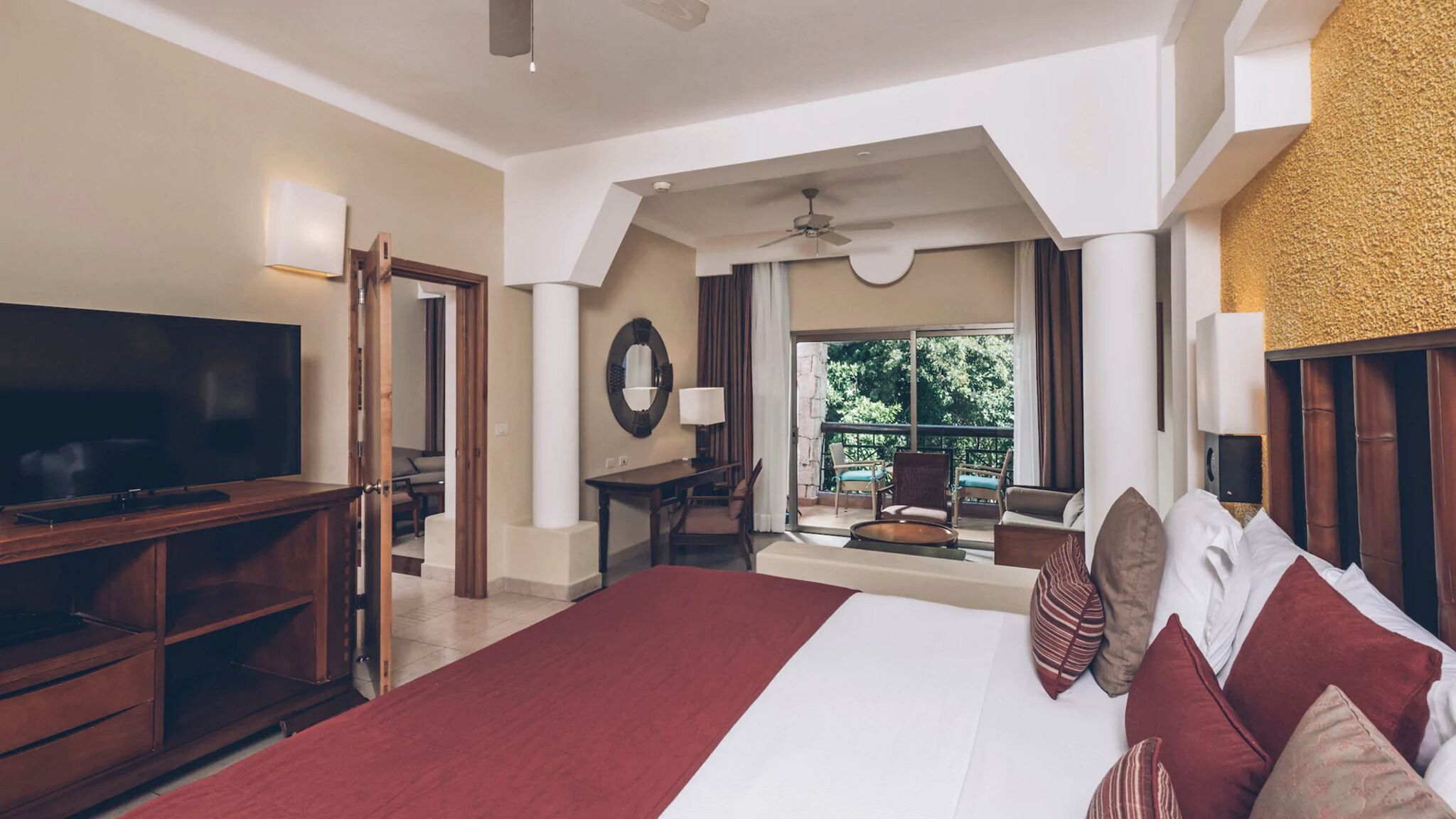 A hotel room with a large bed, a TV, a desk, and a balcony with outdoor furniture.