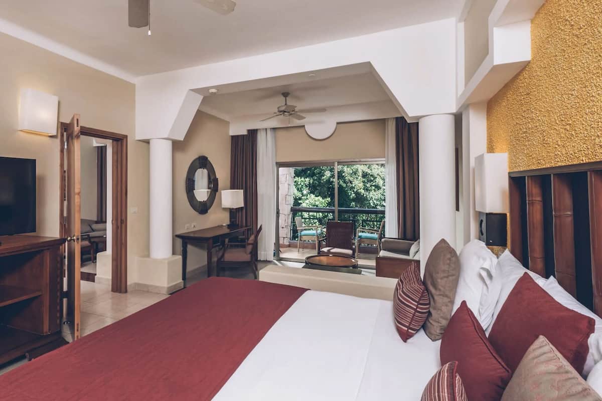 Una habitación de hotel con una cama grande, televisión, escritorio y balcón con mobiliario exterior.