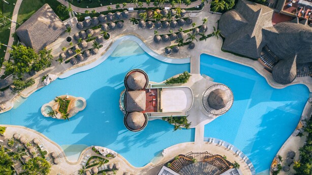 An aerial view of a resort with multiple swimming pools, sun loungers, and palm trees.