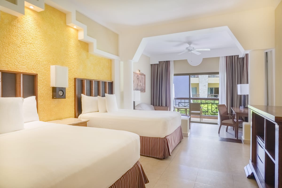 A hotel room with two beds, a desk, a chair, a TV, and a balcony with a view.