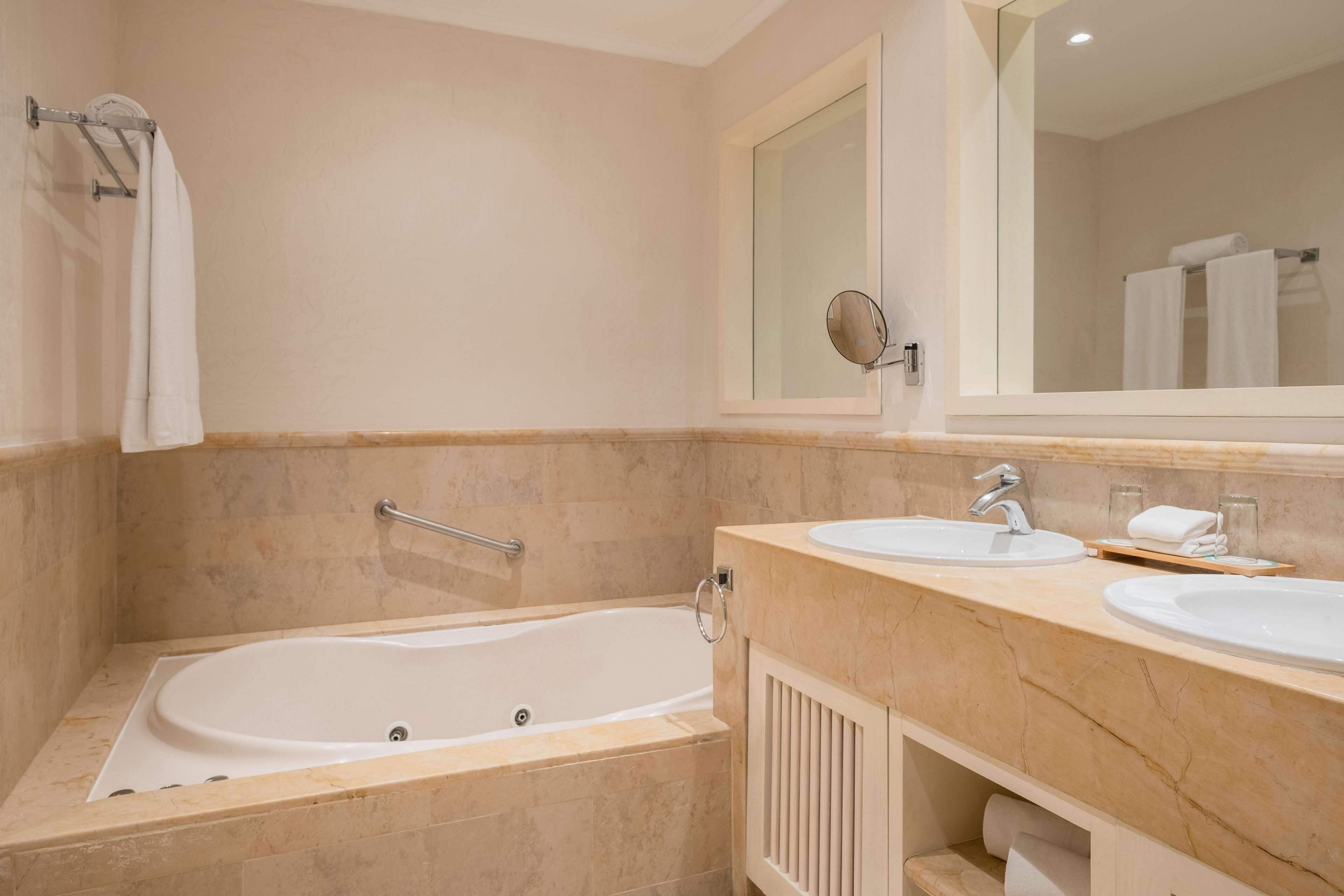 A modern bathroom with a bathtub, two sinks, a mirror, and a towel rack.