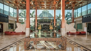 A spacious lobby with a glass coffee table, red cushioned seating, and a view of a pyramid-like structure outside.