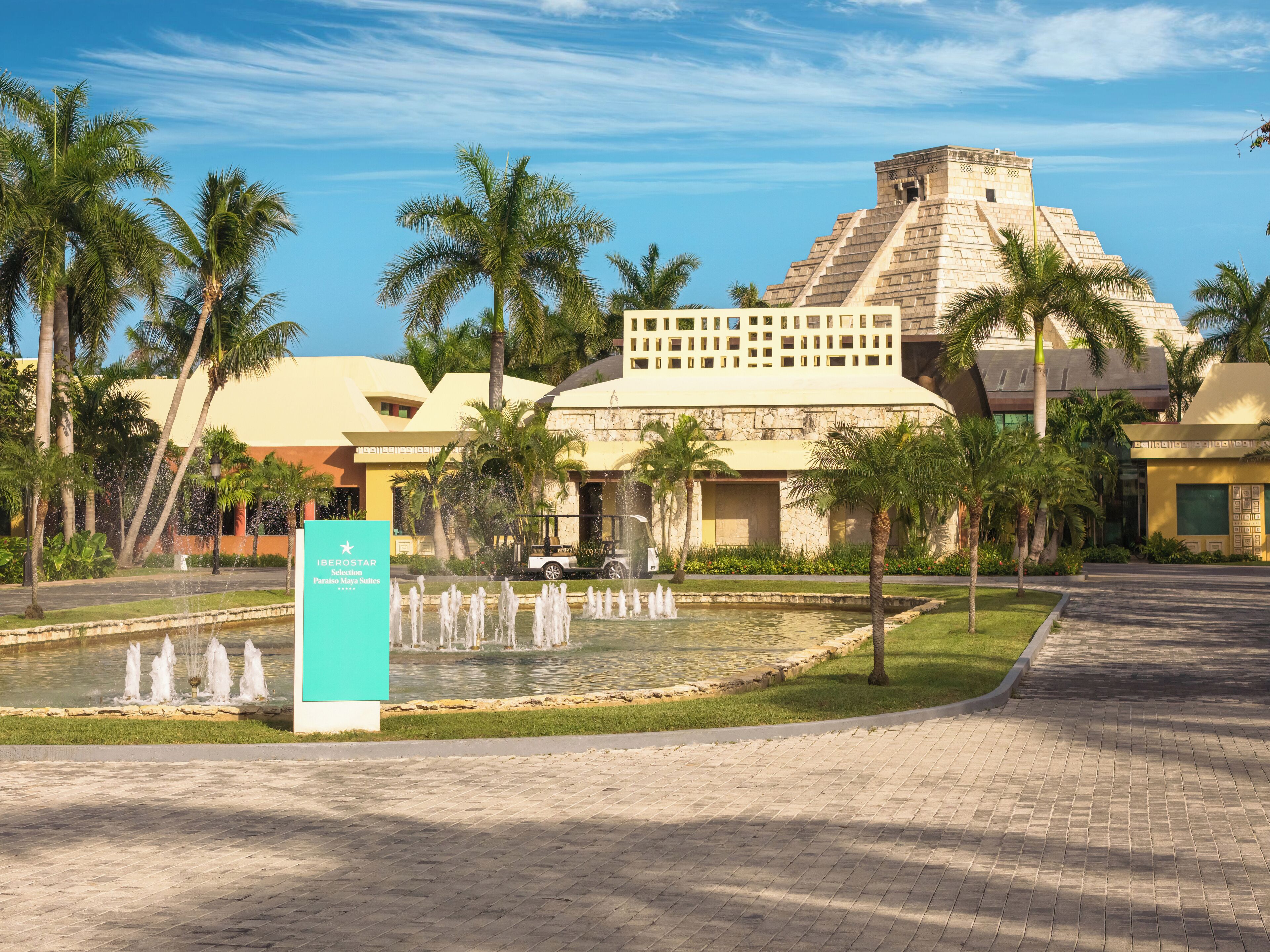 Un resort con un edificio en forma de pirámide, palmeras y una fuente.
