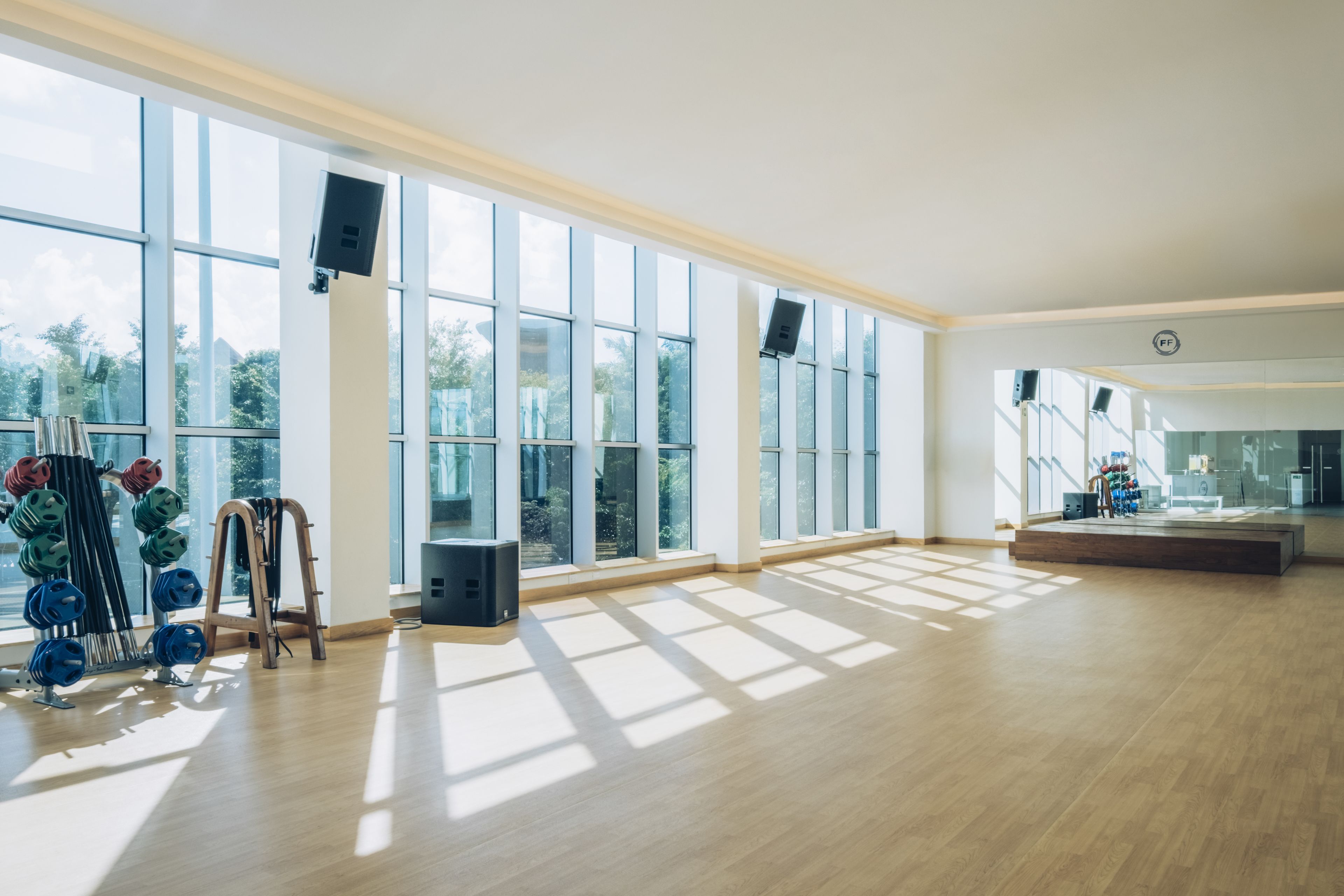 A spacious gym with large windows, weightlifting equipment, and a wooden floor.