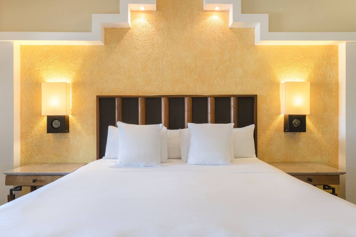 A hotel room with a large bed, two bedside tables, and wall-mounted lamps.