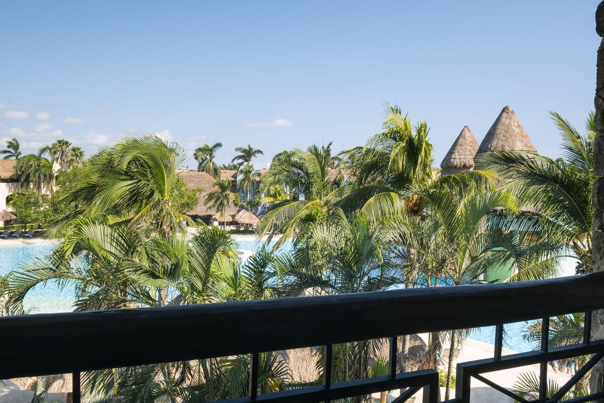 A resort with a pool, palm trees, and thatched-roof huts.
