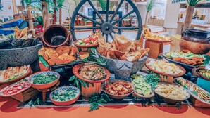 A buffet table with various dishes and a large decorative wheel in the background. - Iberostar Selection Paraíso Lindo - All Inclusive (Playa del Carmen)
