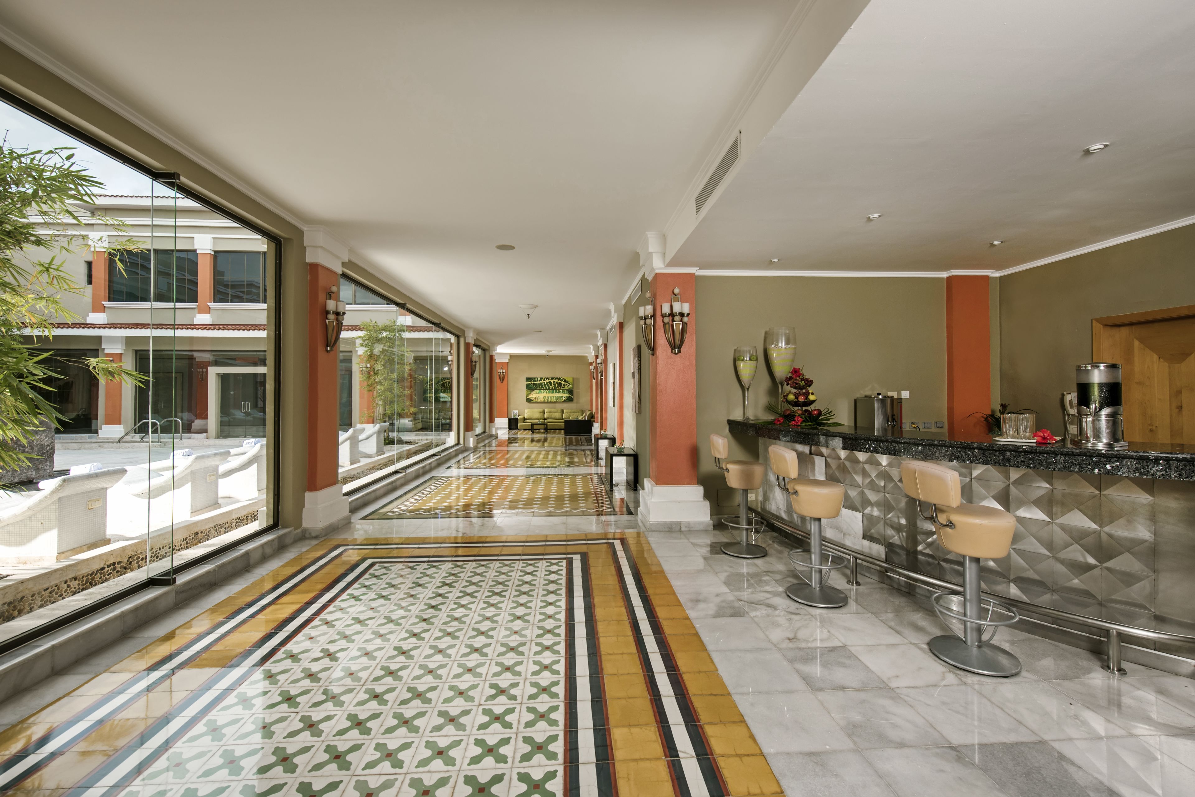 Un hall de hotel con un largo pasillo, una zona de bar con taburetes y un suelo estampado.