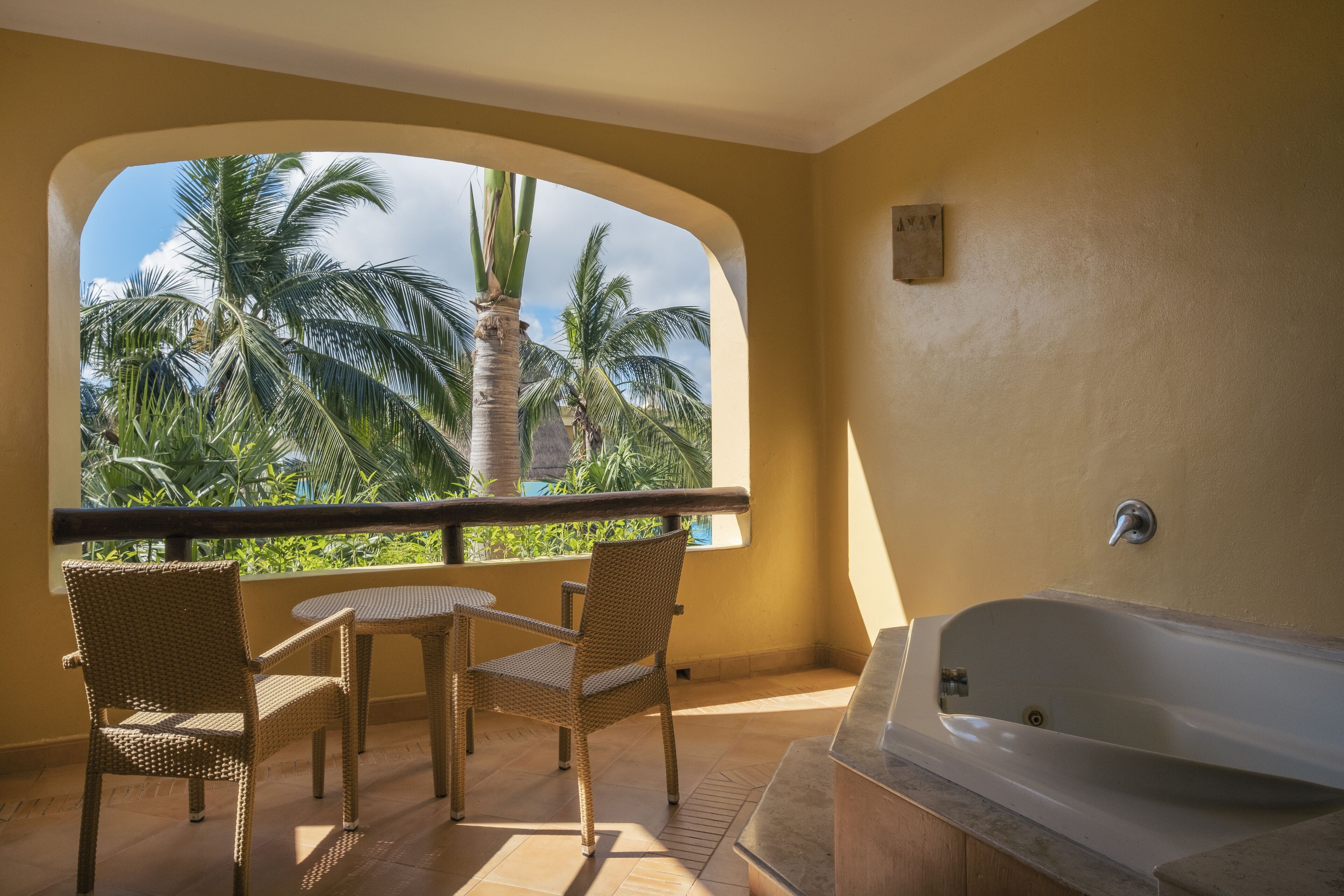 A balcony with wicker chairs, a view of palm trees, and a bathtub.