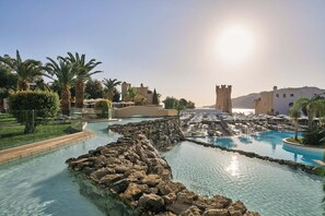 A resort pool area with clear water, palm trees, and a castle-like structure in the background.