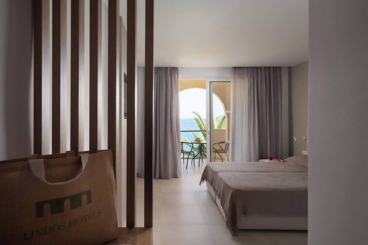 A hotel room with a bed, a chair, a table, and a view of the ocean.