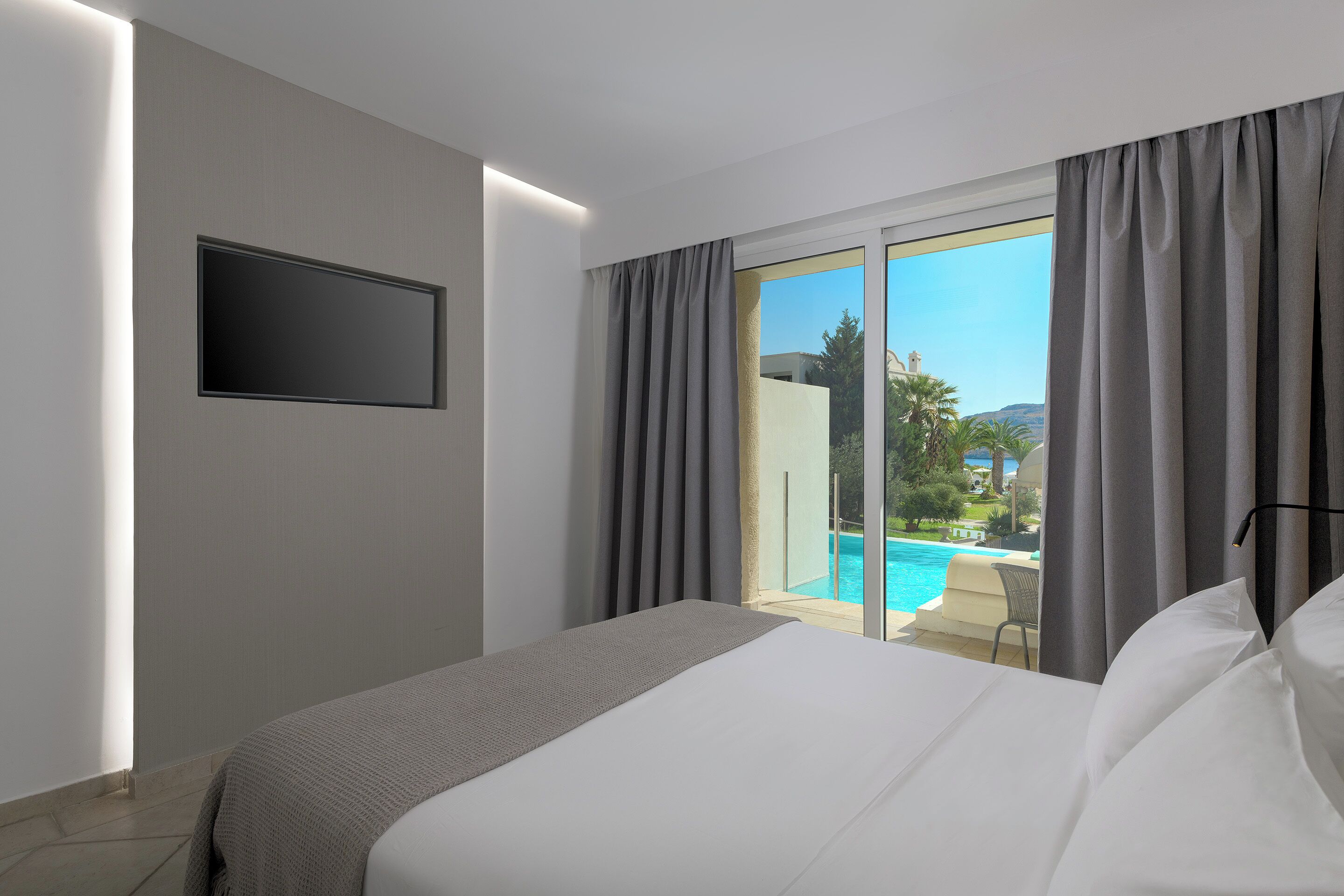 Una camera d'albergo con un letto, una TV a schermo piatto montata a parete e vista su una piscina dalla finestra.