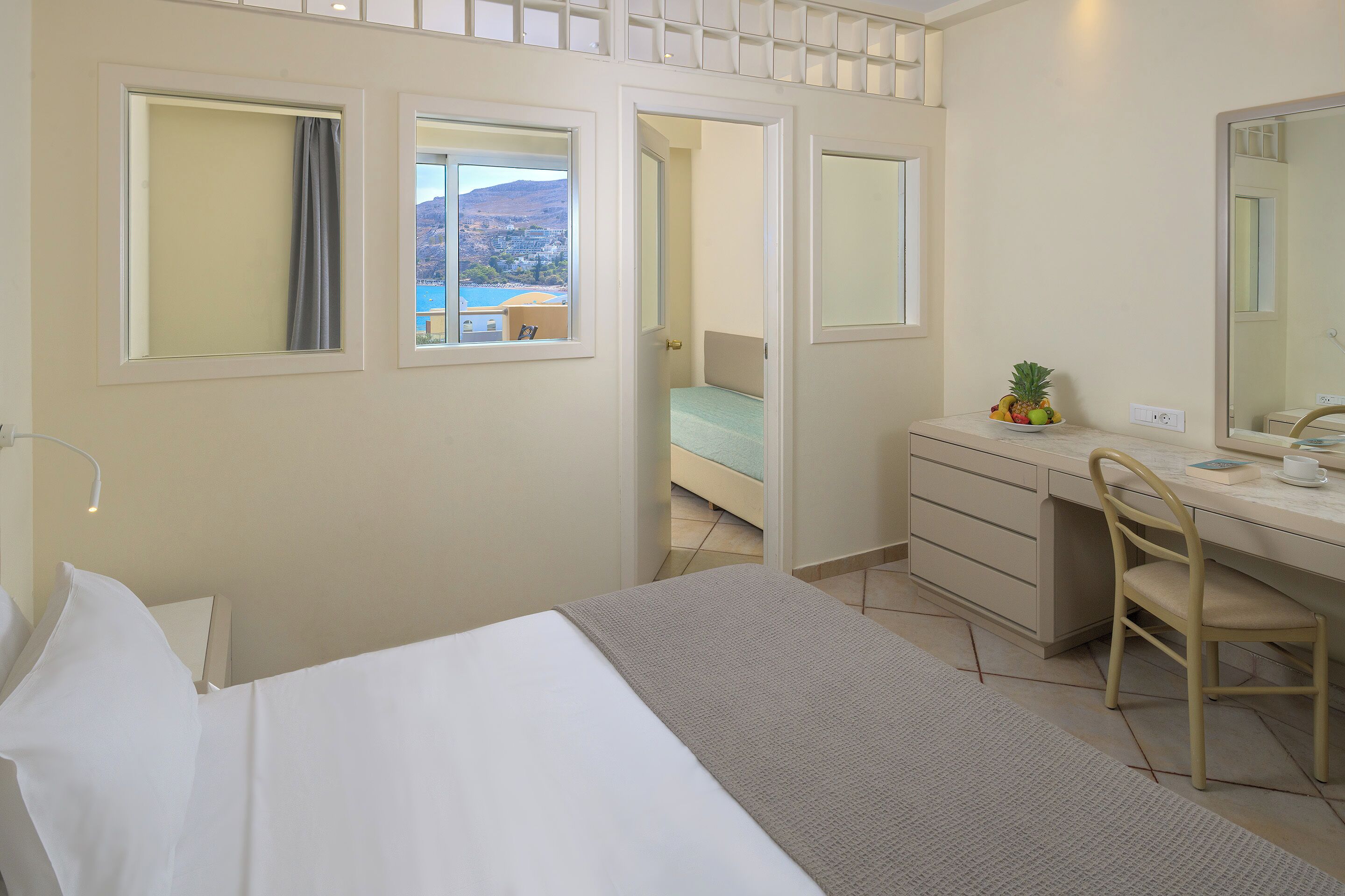 A hotel room with a bed, a desk with a chair, a mirror, and a view of the outside.