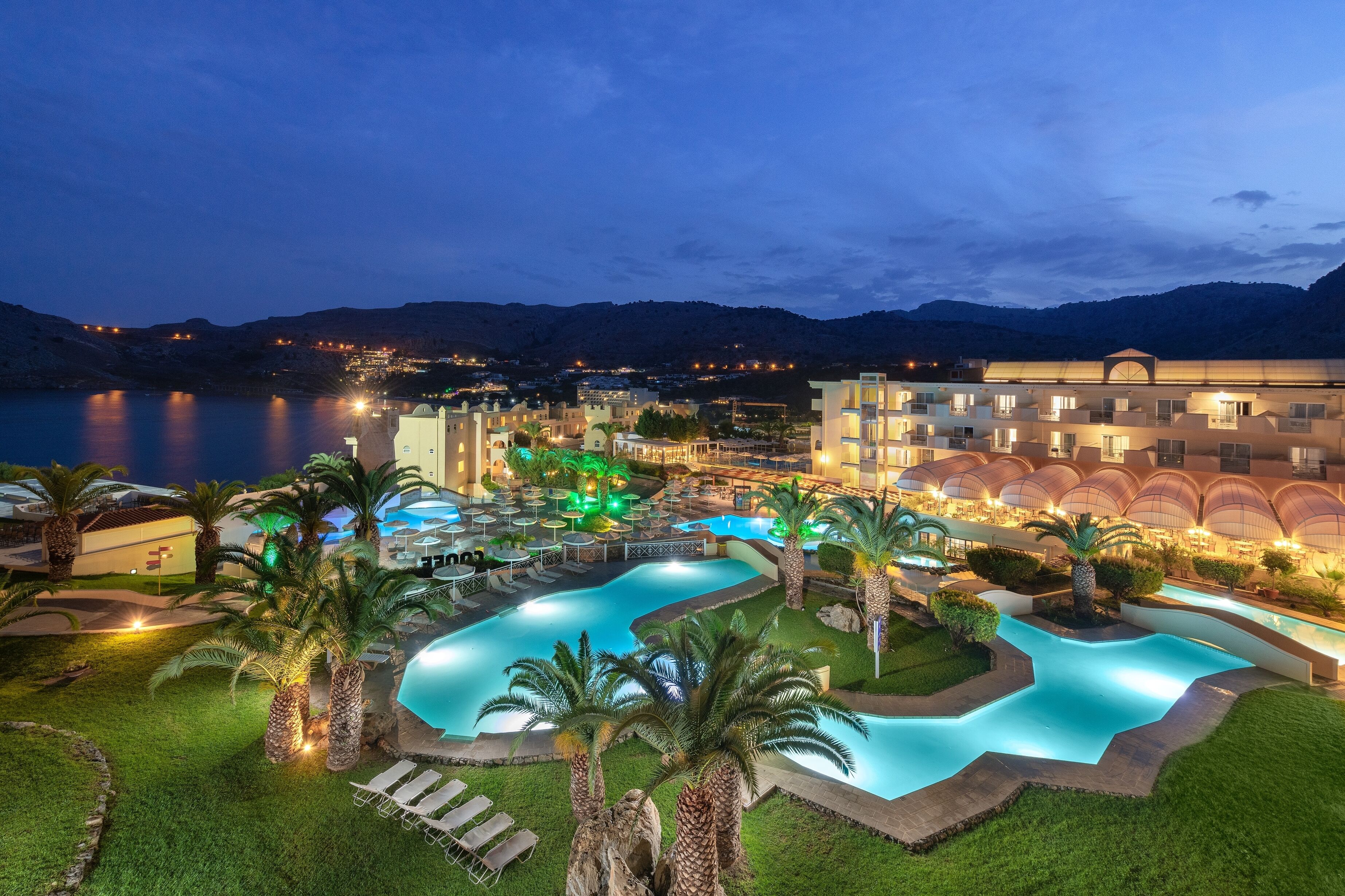 A resort with a swimming pool, palm trees, and a view of the mountains.