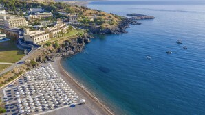 An aerial view of a coastal hotel with a beach area, multiple buildings, and boats in the water.
