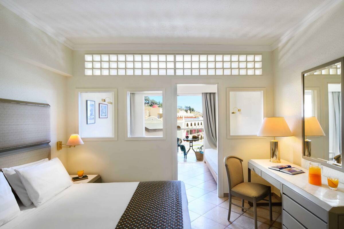 A hotel room with a bed, a desk, a chair, and a large window.