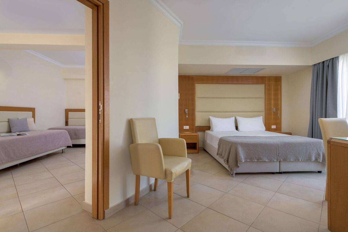 A hotel room with two beds, a chair, a desk, and a wardrobe.