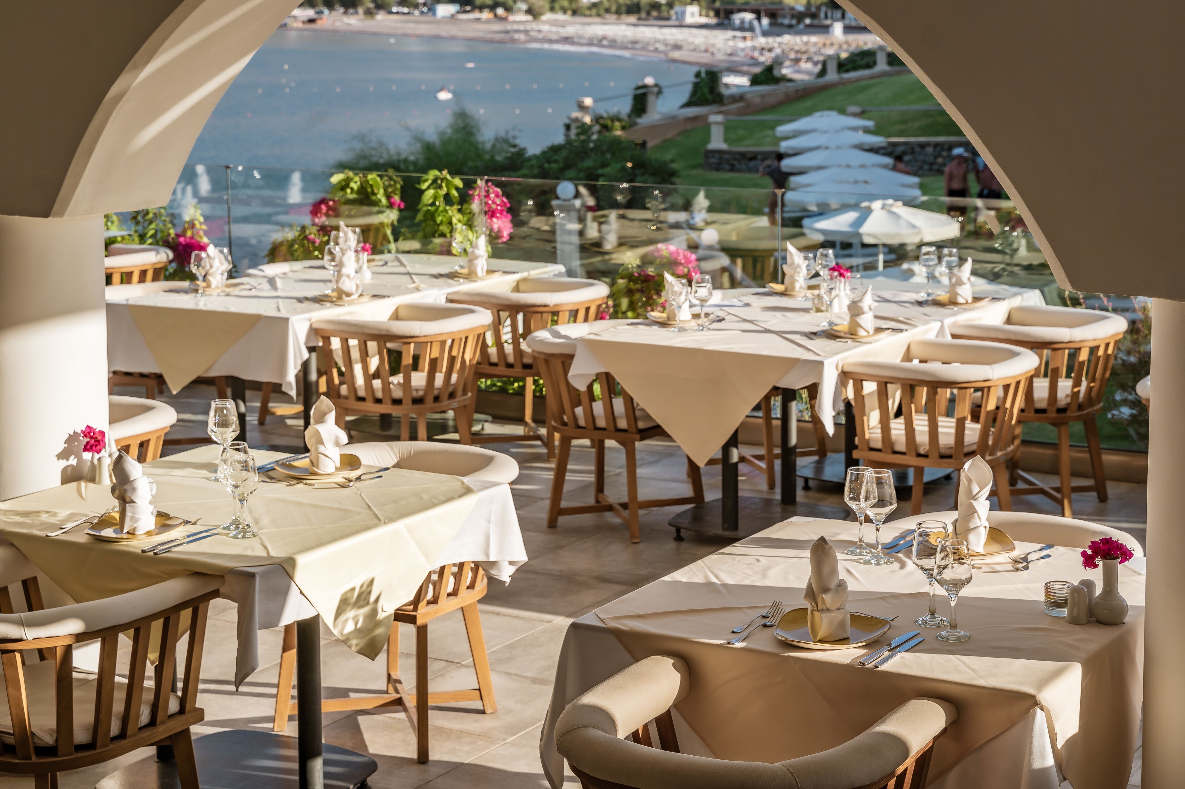 Un espace repas avec des tables dressées pour le repas, offrant une vue panoramique sur un plan d’eau et une végétation luxuriante.