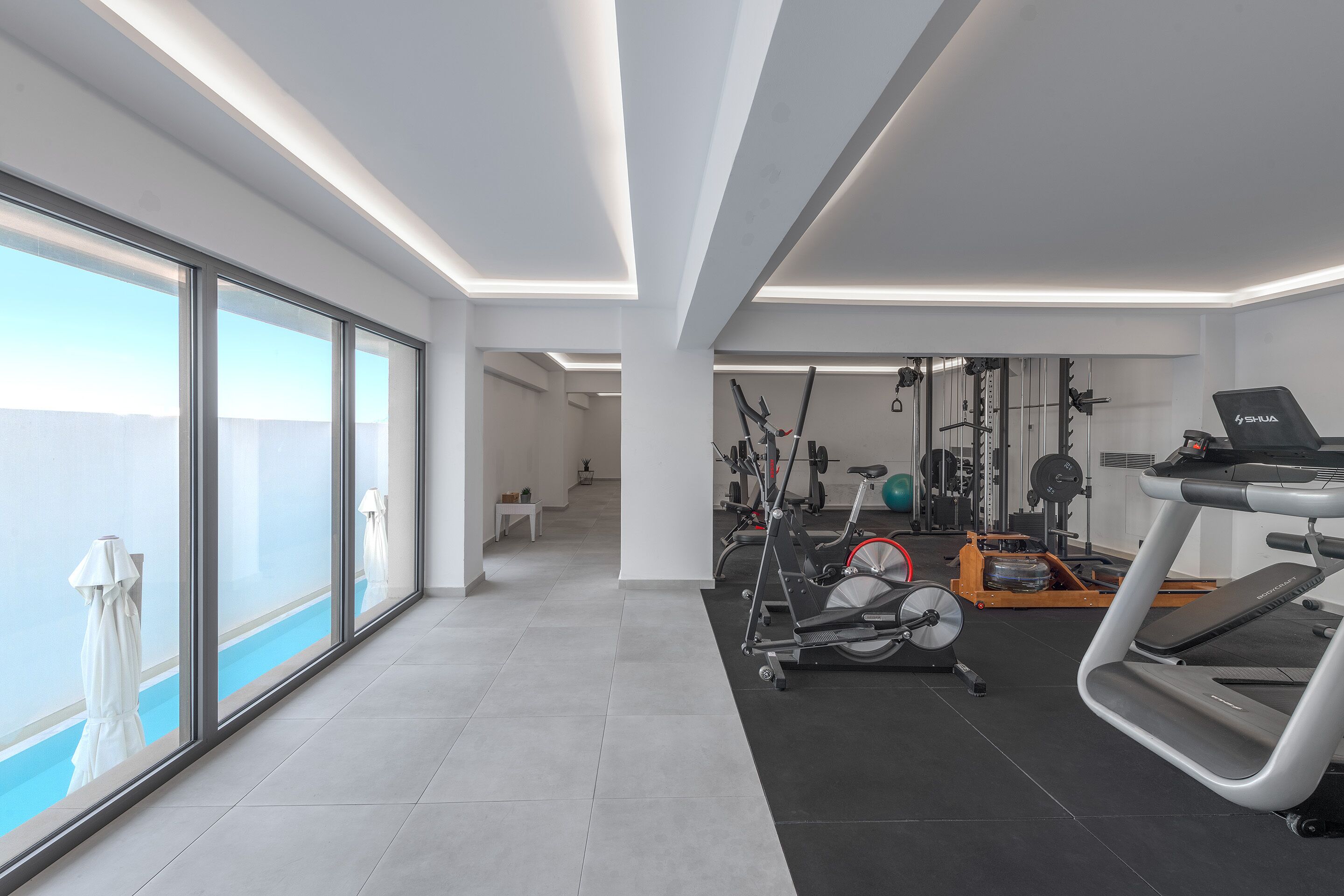 Un gimnasio moderno con equipamiento de ejercicio, amplias ventanas y vistas al cielo.