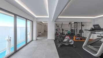 Un gimnasio moderno con equipamiento de ejercicio, amplias ventanas y vistas al cielo.