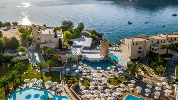 A resort with a large pool, outdoor seating, and a view of the sea.