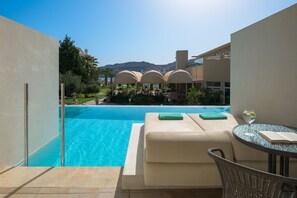 A poolside area with a lounge chair, a glass table with a book and a glass of water, and a view of the pool and distant mountains.