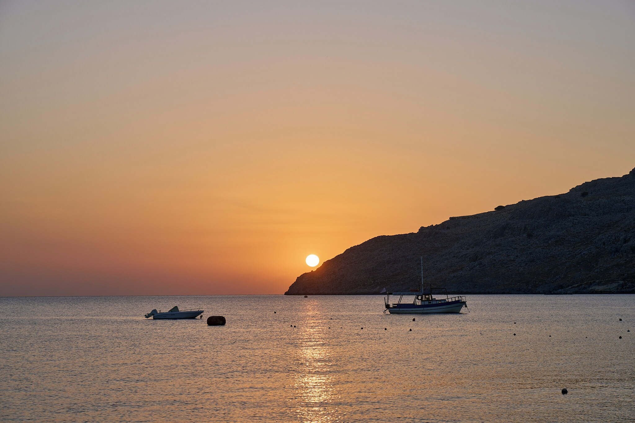 A sunset over a calm sea with two boats anchored.
