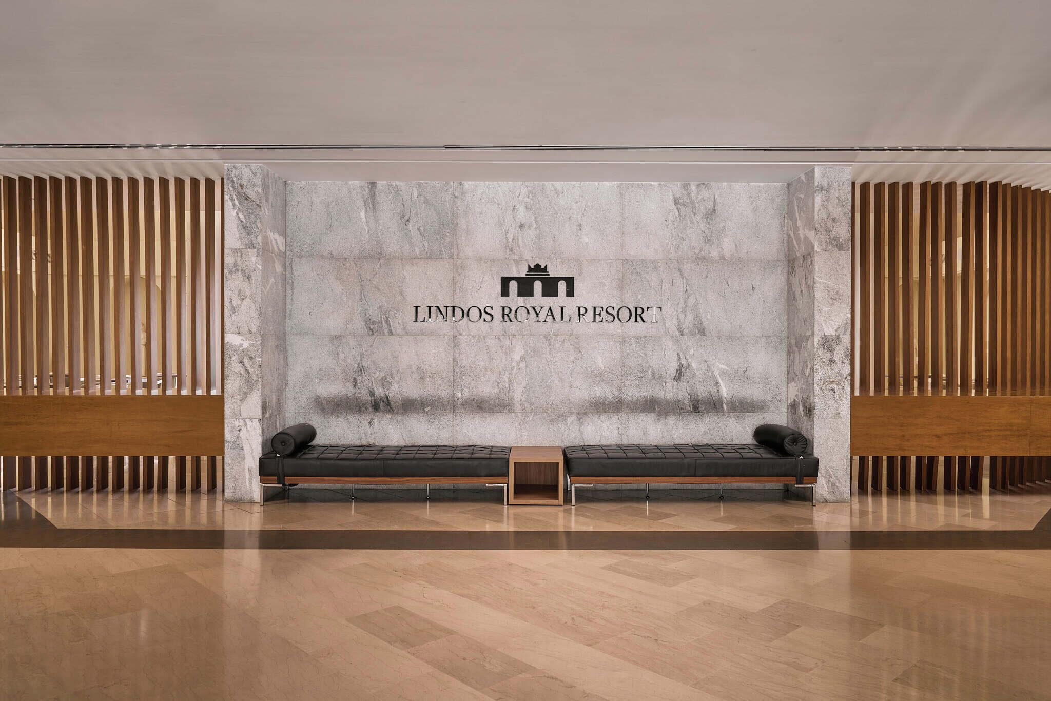 A modern lobby with a marble wall, two black sofas, and a wooden slatted wall on either side.