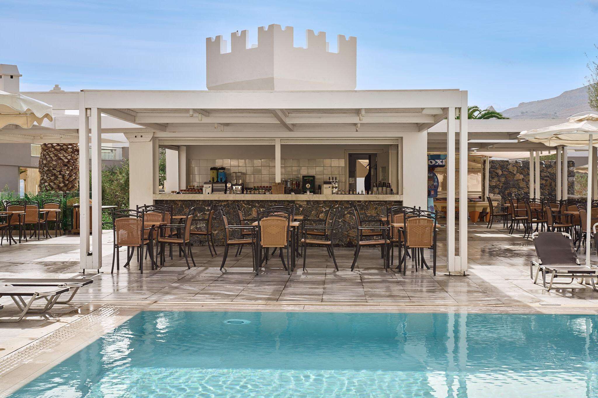 A poolside bar area with a stone wall, bar counter, and seating.
