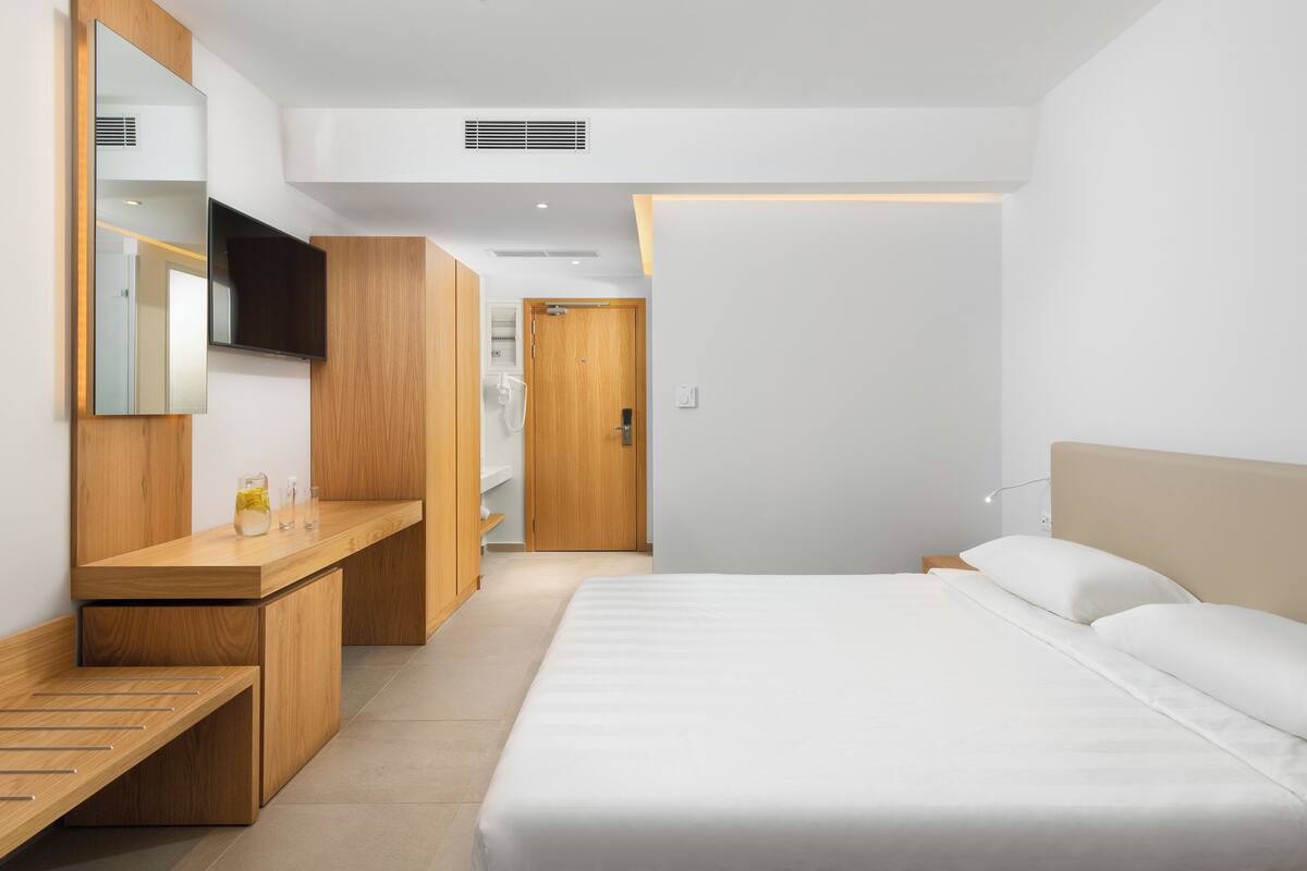 A modern hotel room with a wooden vanity, a bed with white linens, and a large mirror.