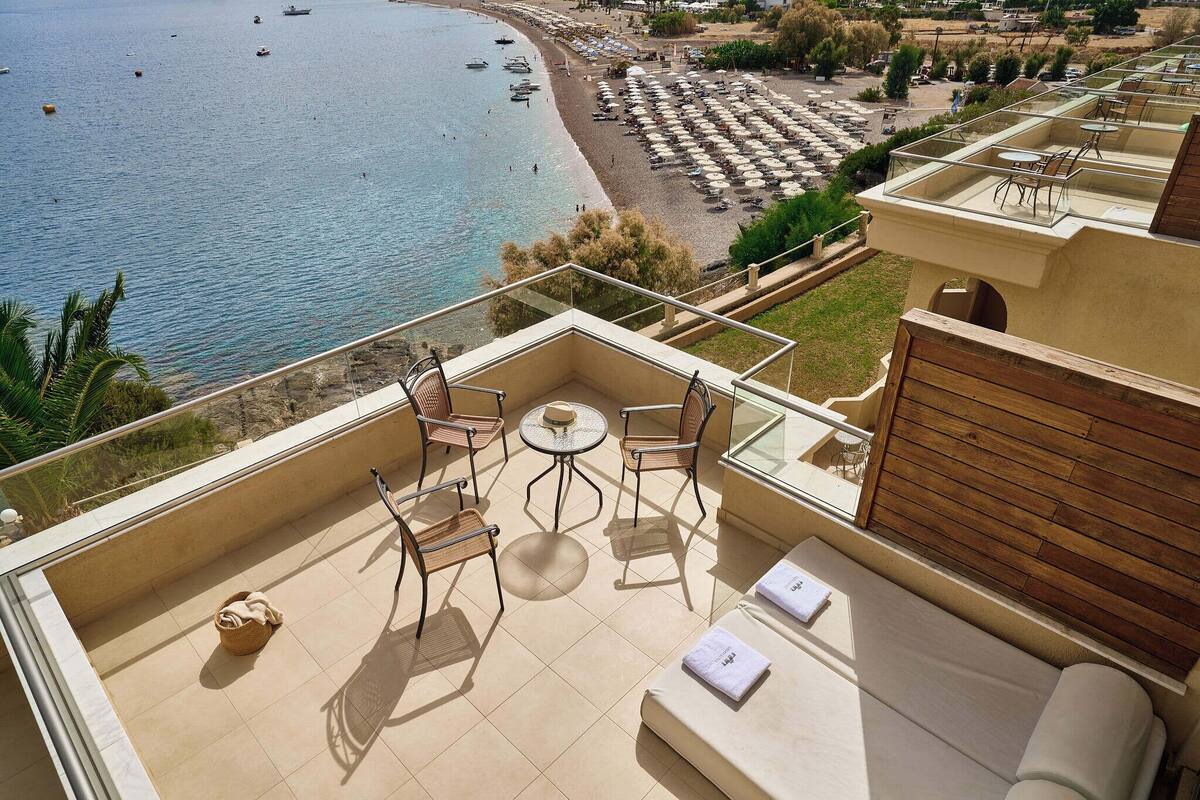 A balcony with a view of the sea, a small table, two chairs, and a sofa.