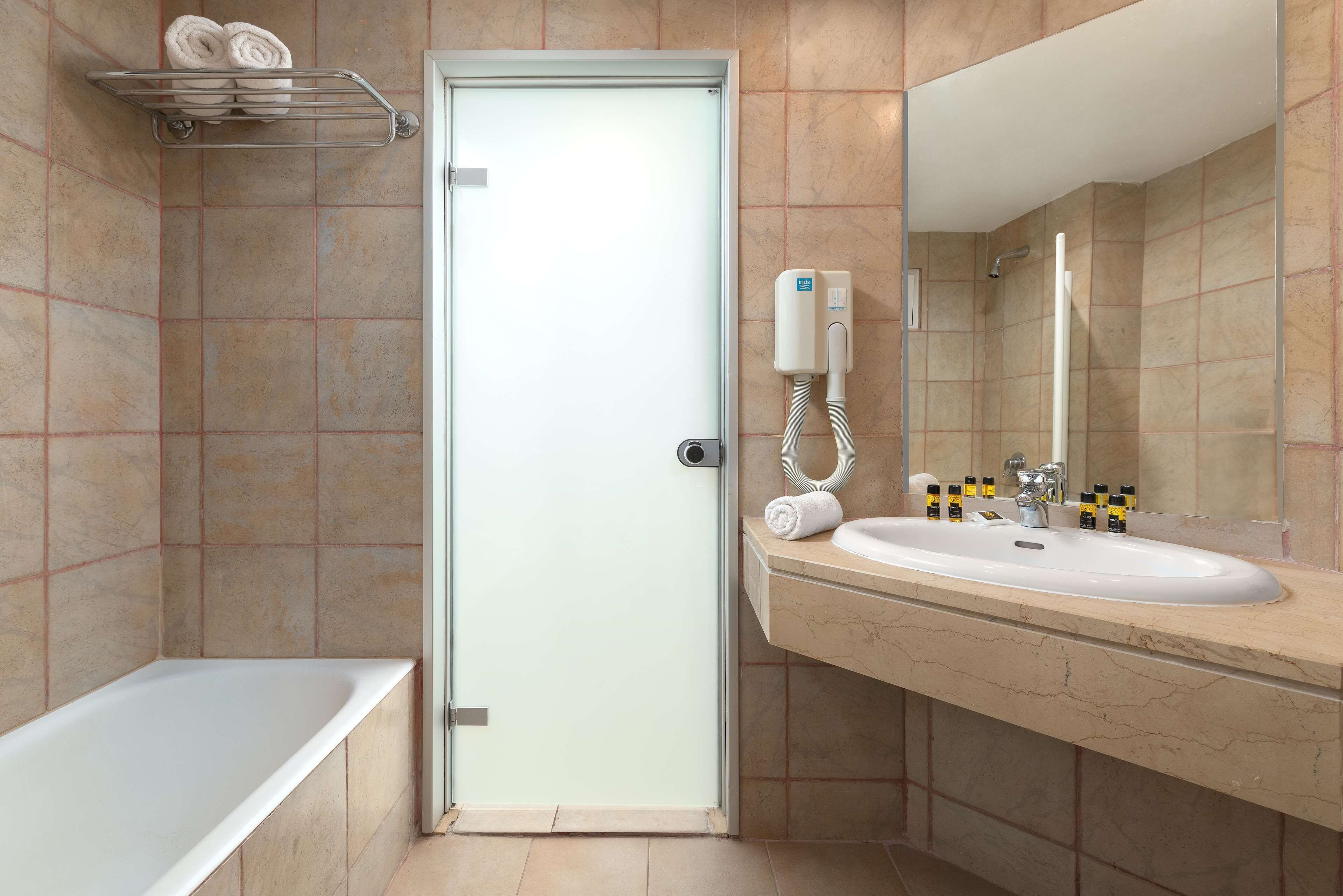 Un baño moderno con puerta de vidrio, una bañera, un lavamanos con espejo y un perchero para toallas.