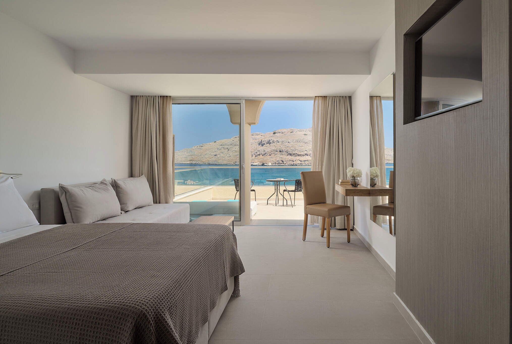 Habitación de hotel con cama, zona de estar con mesa y sillas, y balcón con vista al mar.