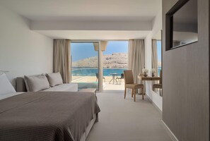 Habitación de hotel con cama, zona de estar con mesa y sillas, y balcón con vista al mar.
