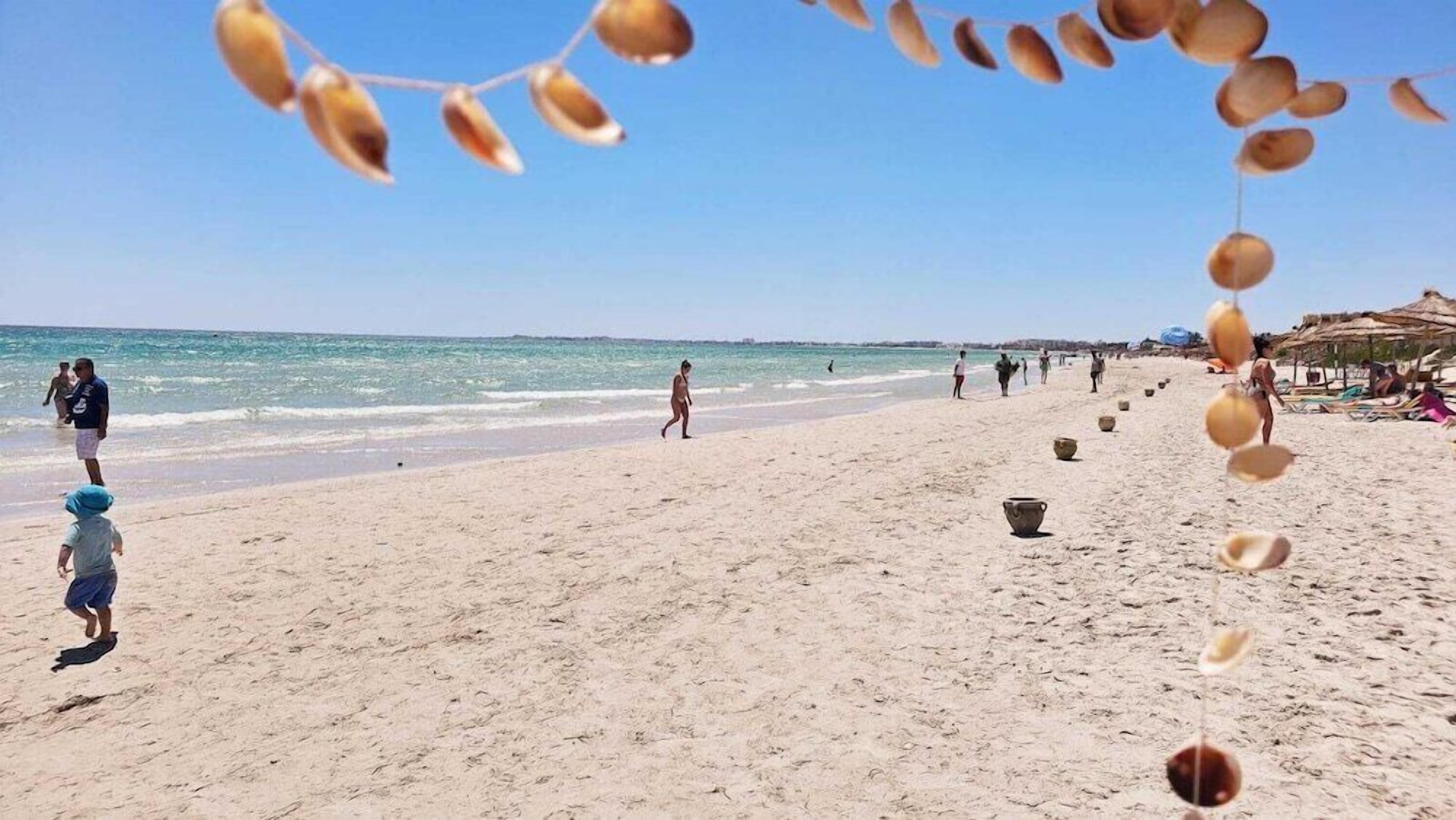 Une plage où l’on voit des gens se promener, des parasols et des activités proposées au bord de la mer.