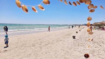 Une plage où l’on voit des gens se promener, des parasols et des activités proposées au bord de la mer.