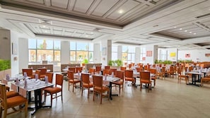A spacious dining area with multiple tables and chairs, large windows, and a modern ceiling design.