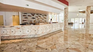 A hotel lobby with a marble reception desk, a stone wall with fish and plant carvings, and a large open space with columns. - Iberostar El Fatimi (Mahdia)