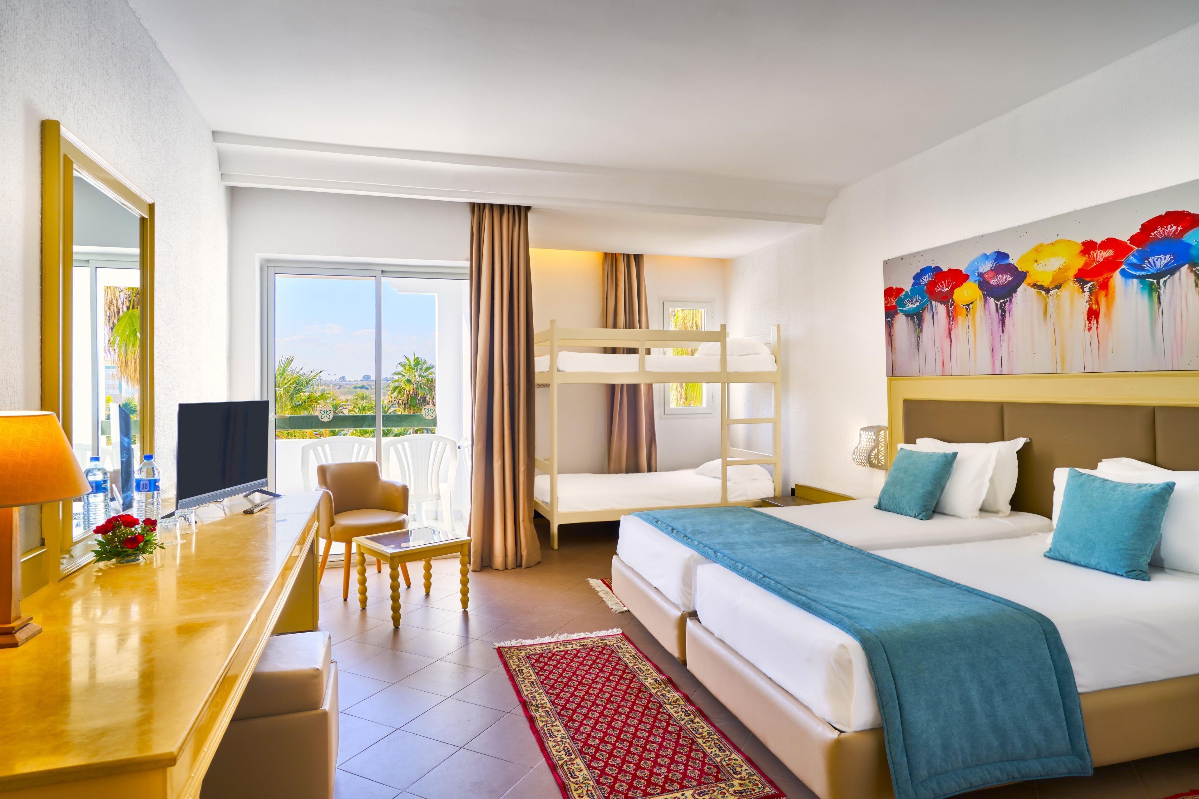 A hotel room with a bed, a desk, a chair, a television, and a window with a view of greenery.