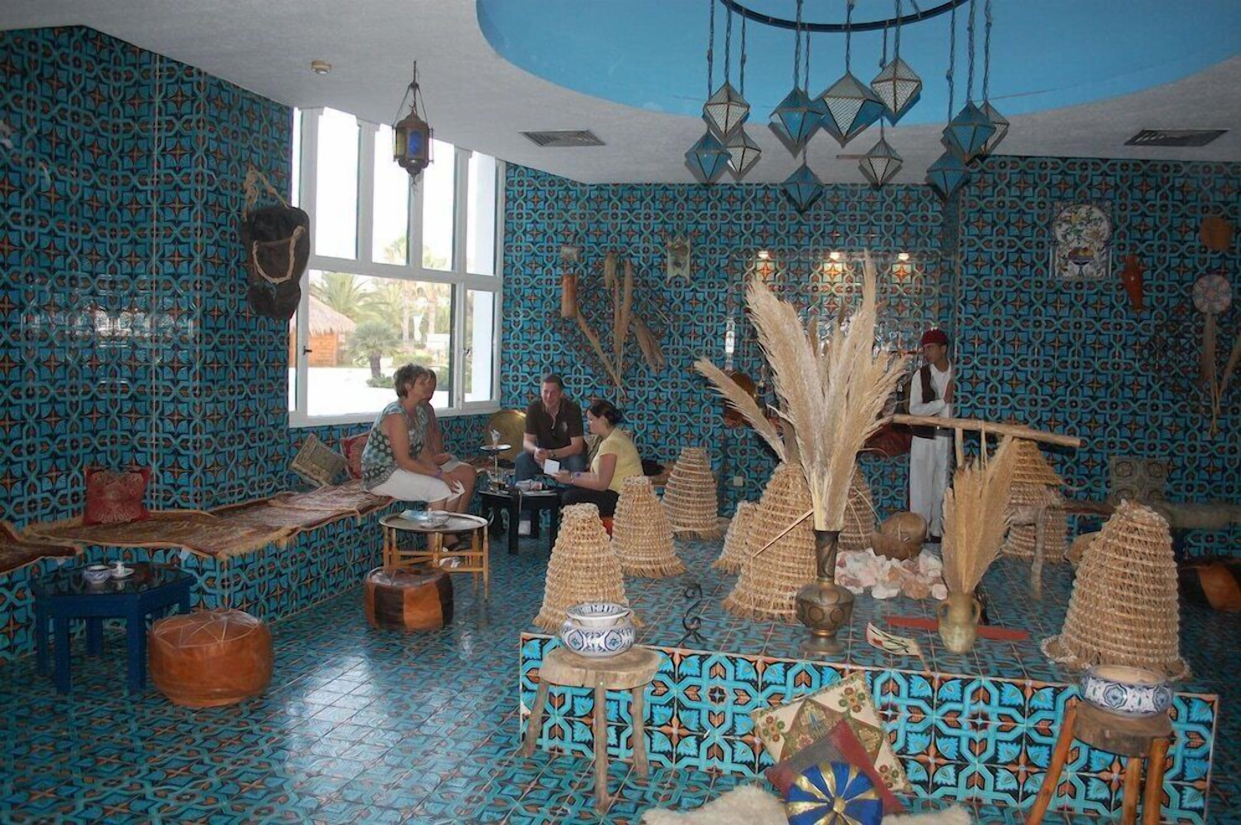 Une pièce aux murs décorés de motifs, avec une grande fenêtre et un espace de détente central comprenant des tables et des chaises.