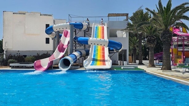 A pool with two water slides, one with a pink and white pattern and another with a rainbow design. - Iberostar El Fatimi (Mahdia)