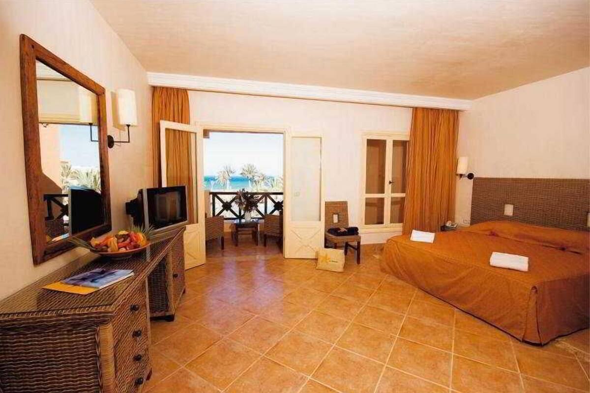 A hotel room with a bed, television, wicker furniture, and a view of the outdoors.