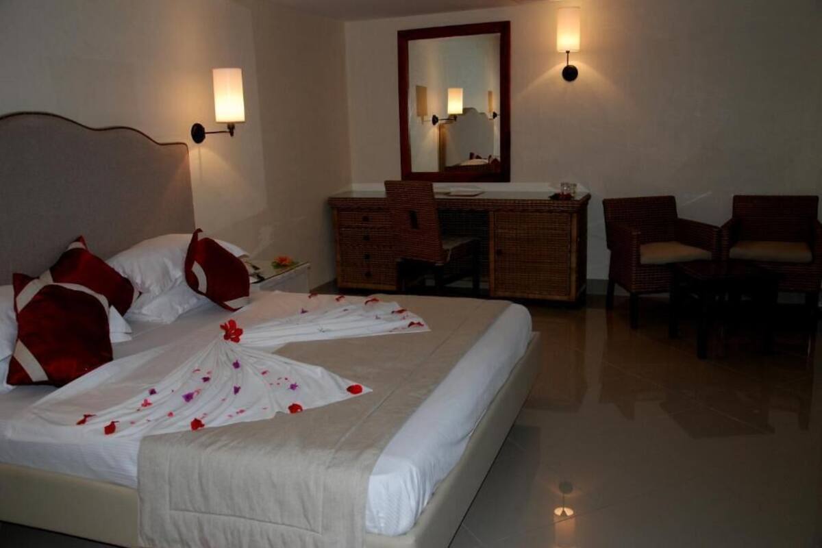 A hotel room with a bed, a desk, two chairs, a mirror, and wall sconces.