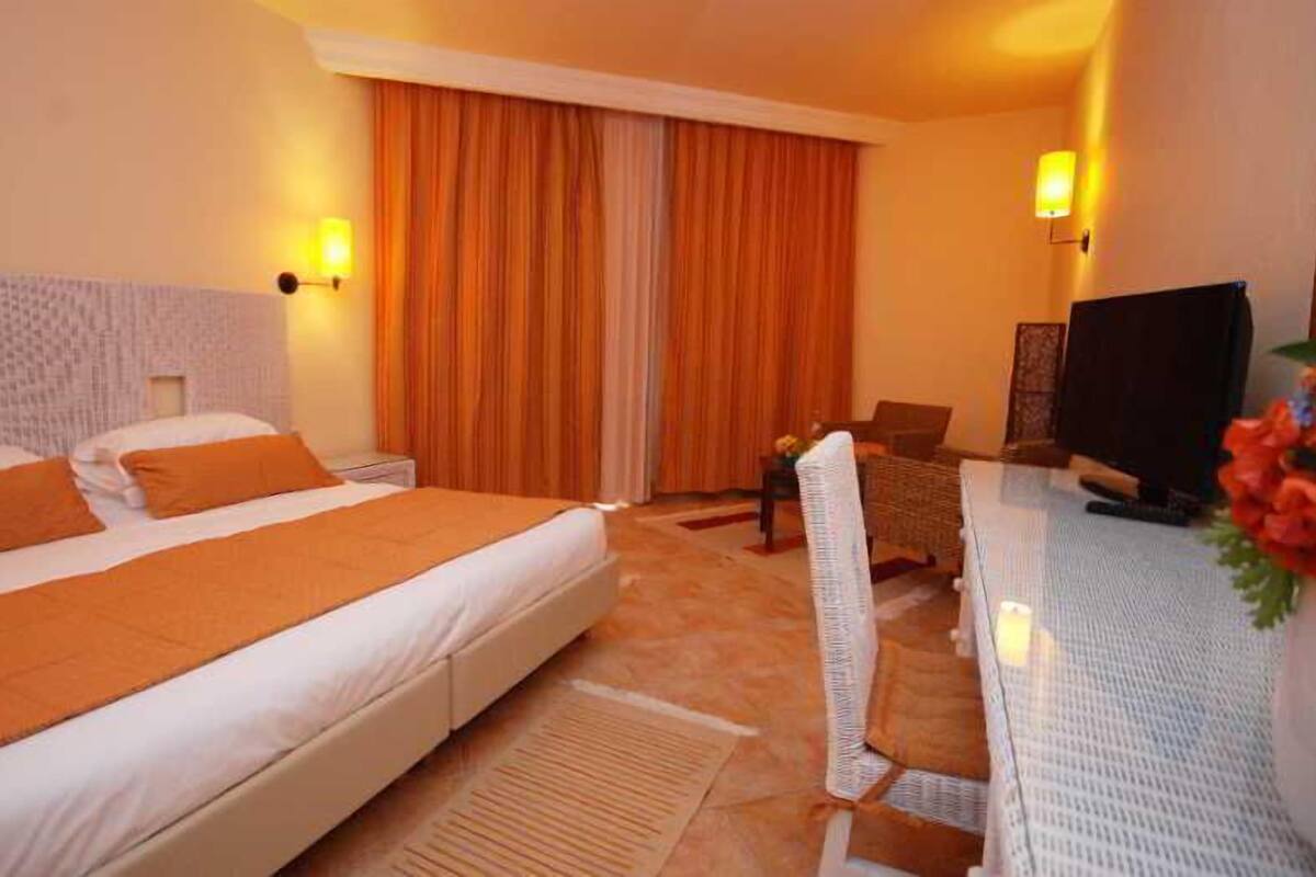 A hotel room with a bed, a desk with a chair, a television, and a window with curtains.