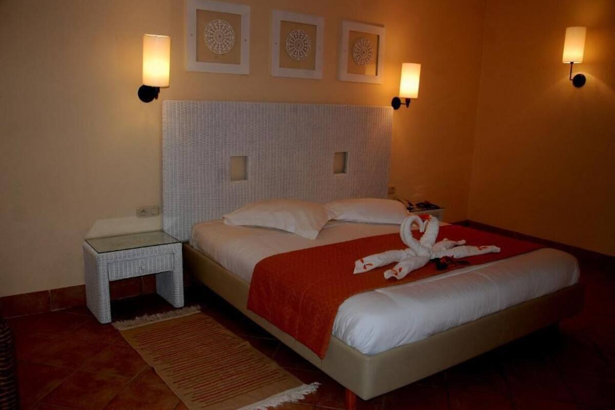 A hotel room with a large bed, a nightstand, a wall-mounted lamp, and a decorative wall piece.