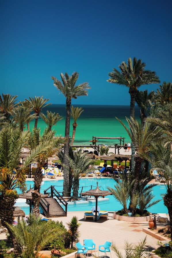 A resort pool area with palm trees, lounge chairs, and a view of the ocean. - Vincci Safira Palms (Zarzis)